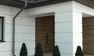 Nowoczesny dom z białym boniowaniem, drewnianymi drzwiami i ozdobnymi elementami elewacji.