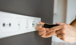 Ręce majsterkowicza przykręcają śrubokrętem gniazdko. Dowiedz się, jak przenieść gniazdko bez kucia, by wygodnie korzystać z prądu.