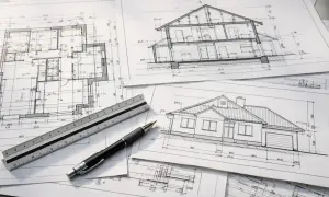 Na stole leżą rysunki architektoniczne: przekrój domu, rzut parteru i elewacja. Obok znajduje się linijka i długopis, gotowe do pracy nad projektem technicznym i budowlanym.