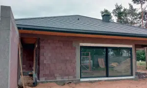 Budowa domu z keramzytu w toku. Widoczna ściana z pustaków, dach i duże okno.