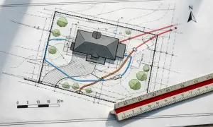 Projekt zagospodarowania działki przykład: plan domu z drogą dojazdową, zielenią i instalacjami. Linijka geodezyjna obok.