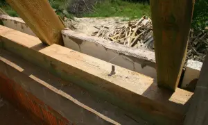 Drewniana więźba dachowa w trakcie budowy, widoczne belki i słupy. Trwa impregnacja więźby dachowej, by chronić drewno przed wilgocią.