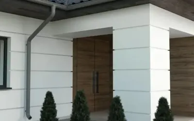 Nowoczesny dom z białym boniowaniem, drewnianymi drzwiami i ozdobnymi elementami elewacji.