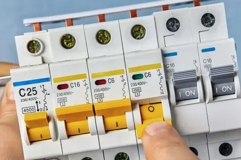 Palec naciska żółty wyłącznik nadprądowy typu b. Obok widać inne zabezpieczenia elektryczne.