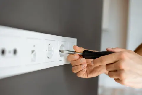 Ręce majsterkowicza przykręcają śrubokrętem gniazdko. Dowiedz się, jak przenieść gniazdko bez kucia, by wygodnie korzystać z prądu.