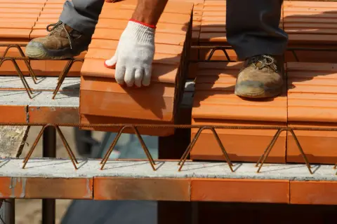 Budowa stropów ceramicznych. Pracownik w rękawicy układa cegły na konstrukcji zbrojeniowej.