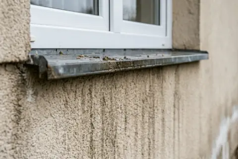 Brudne pionowe pasy na elewacji pod oknem, ślady po deszczu i brudzie.