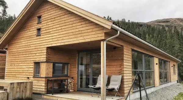 Nowoczesny dom norweski z drewnianą elewacją, tarasem i widokiem na las.