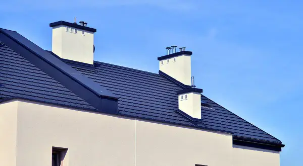 Nowoczesny dach bezokapowy z ciemnogranatową dachówką i białymi kominami, pod błękitnym niebem.