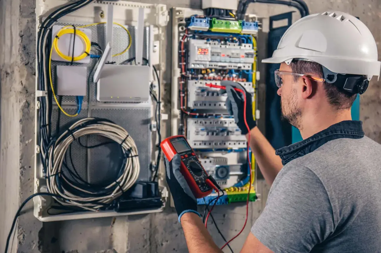 Elektryk sprawdza instalację, dbając o kompensację mocy biernej w domu. W rękach multimetr, w szafie rozdzielczej mnóstwo przewodów.