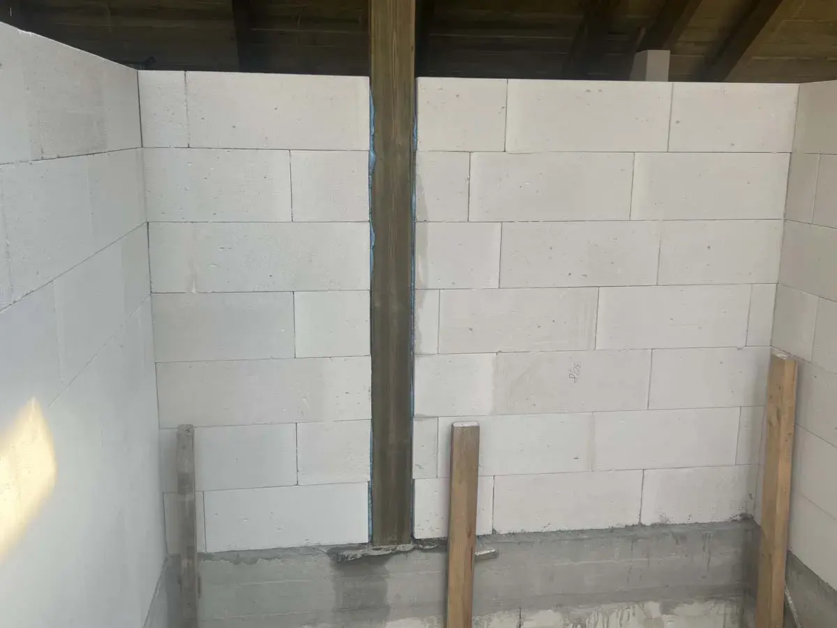 Ściany z bloczków betonowych, widoczne rodzaje dylatacji, pionowy słup drewniany i podpora.