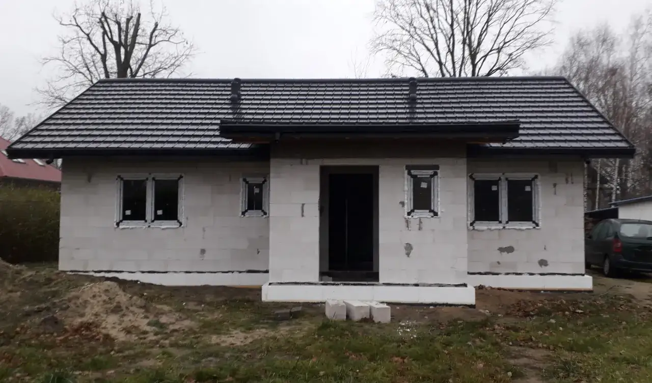 Nowy dom z gankiem w stanie surowym, z szarym dachem i białymi oknami.