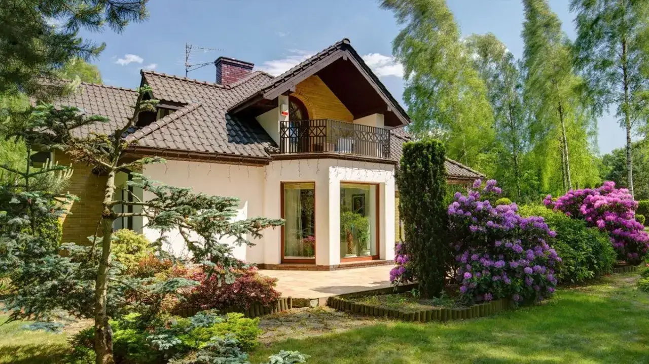 Dom z ryzalitem, balkonem i kwitnącymi rododendronami.