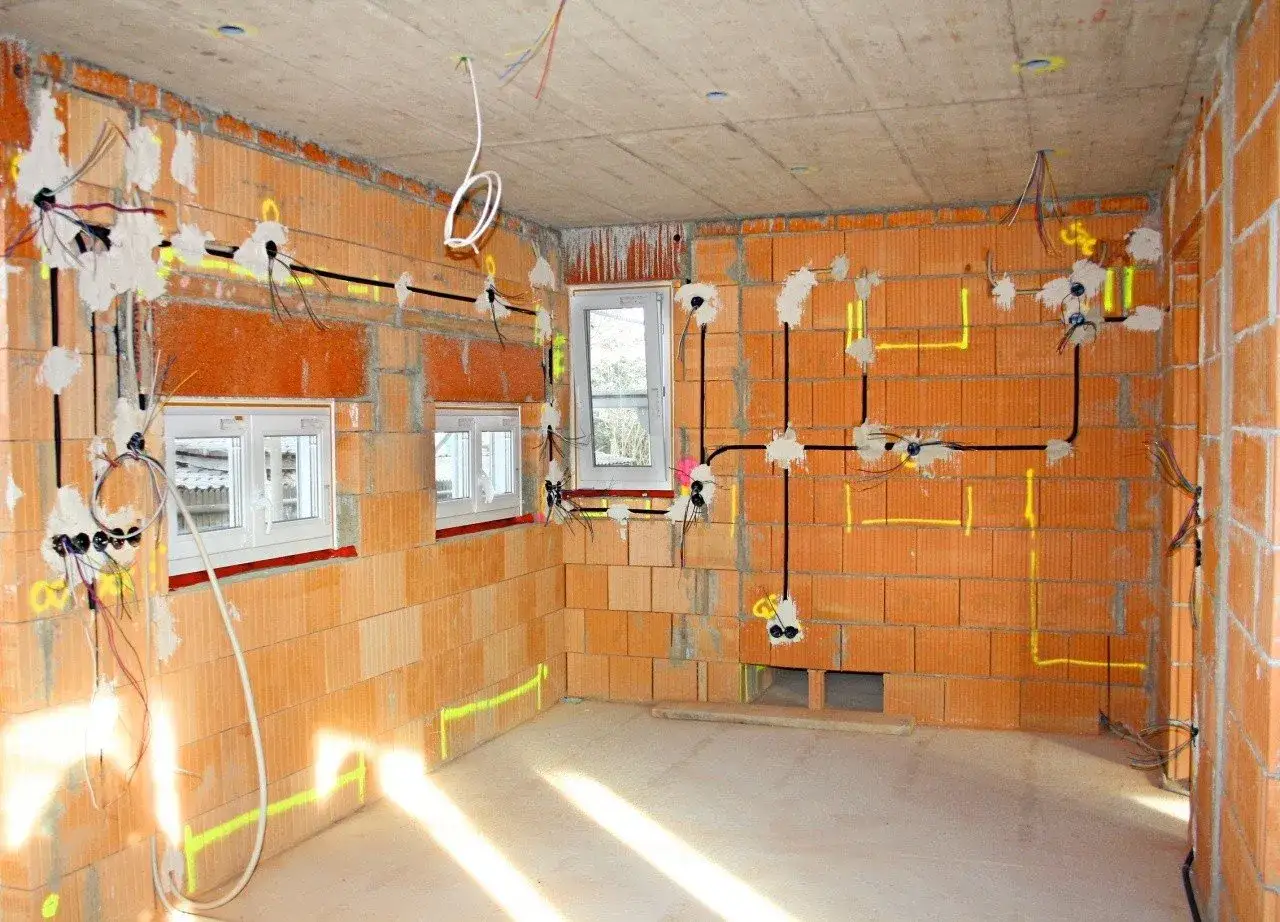 Budowa domu w toku: instalacja elektryczna z przewodami i puszkami, zgodna z normami elektrycznymi. Ściany z cegły, betonowy strop, okna.